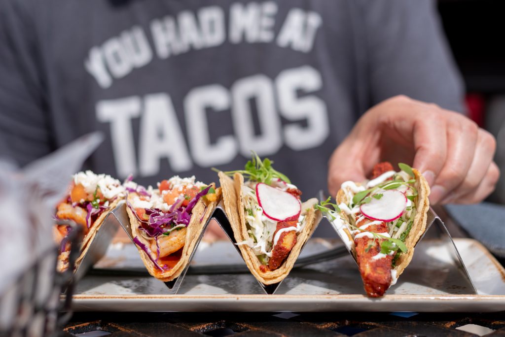 closeup of man eating tacos outside in summer, shirt in background that says you had me at tacos